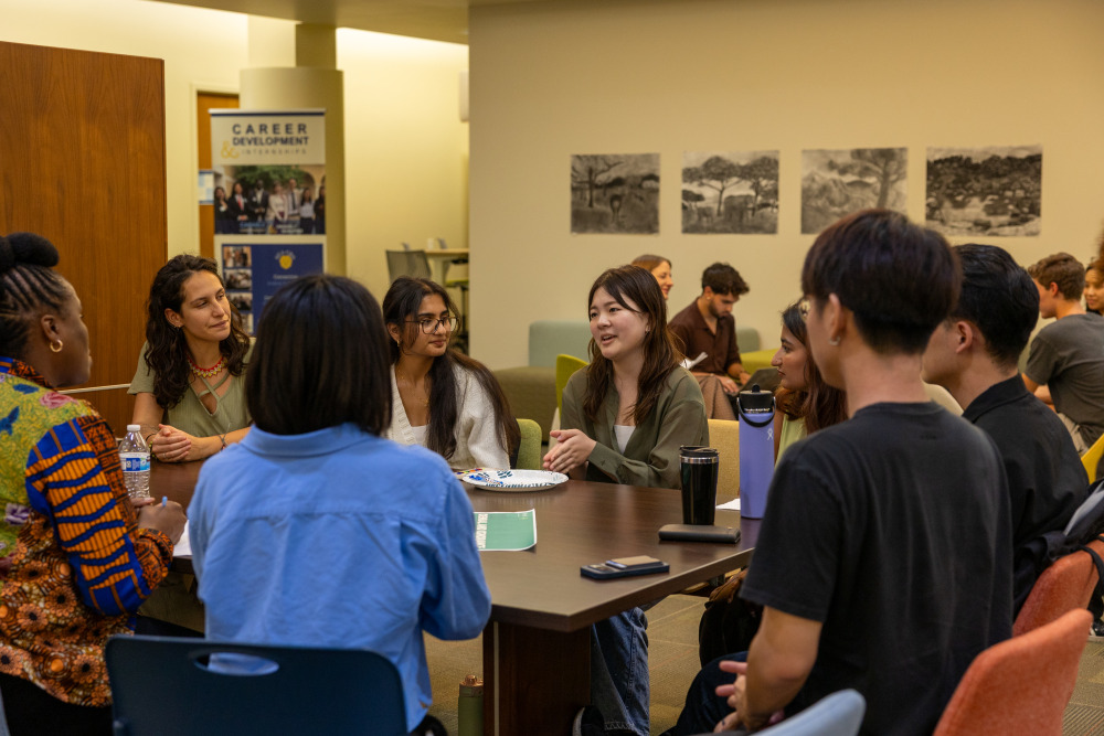 Male and female students sit around a table and participate in a group discussion.