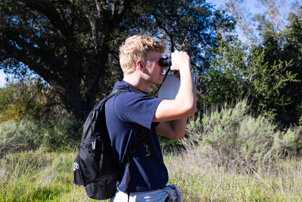 A student with blonde hair using the binoculars