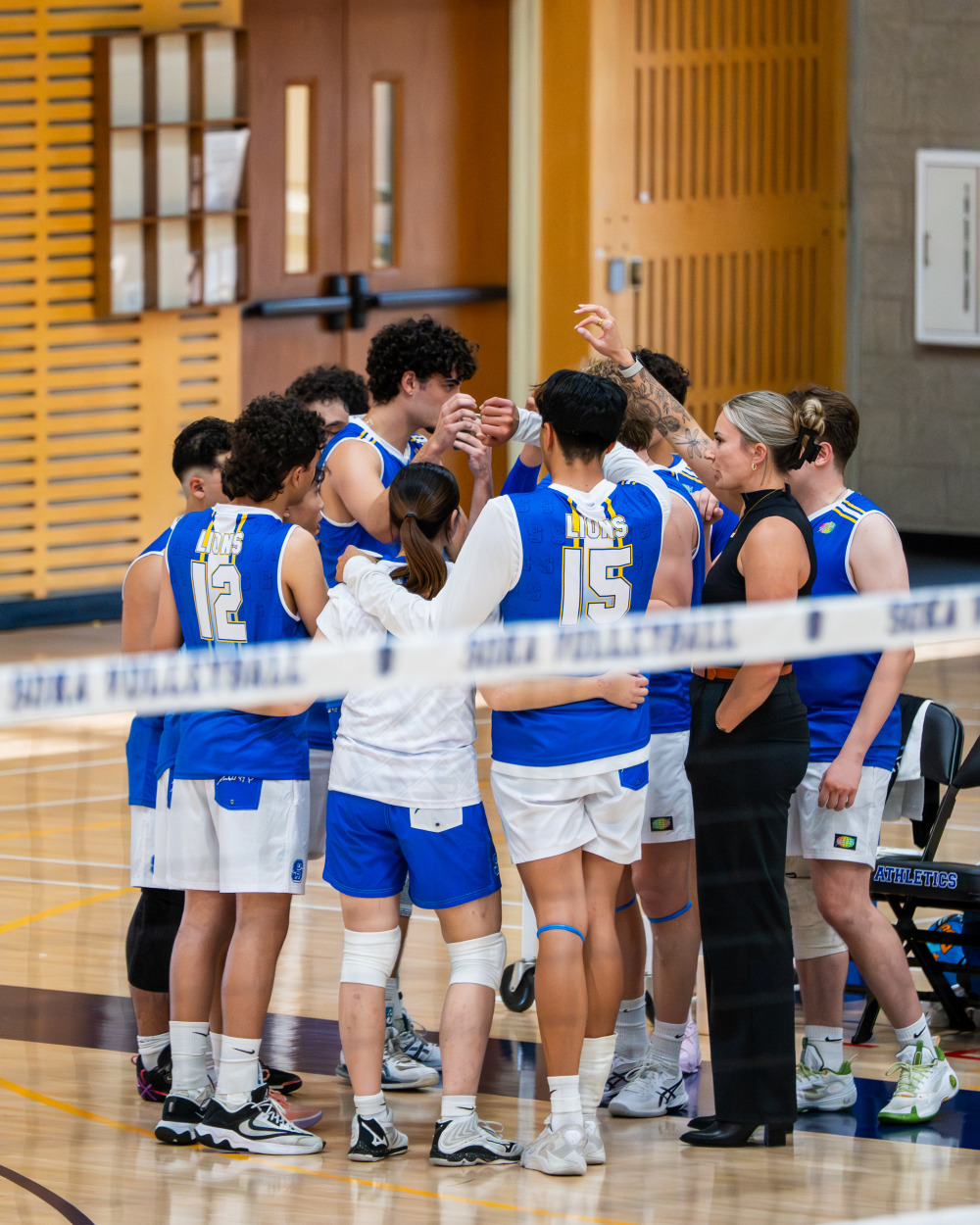 Soka Men's Volleyball players and coaches stand in a huddle with their arms around eachother.