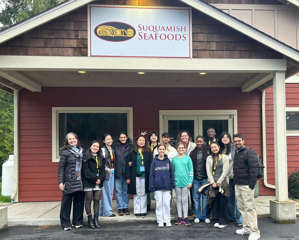 A large group of people pose for a photo in front of the Suquamish Seafoods building, a red wooden structure with a white sign above the entrance.