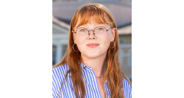 Tess Aman wears glasses and a blue shirt in a headshot