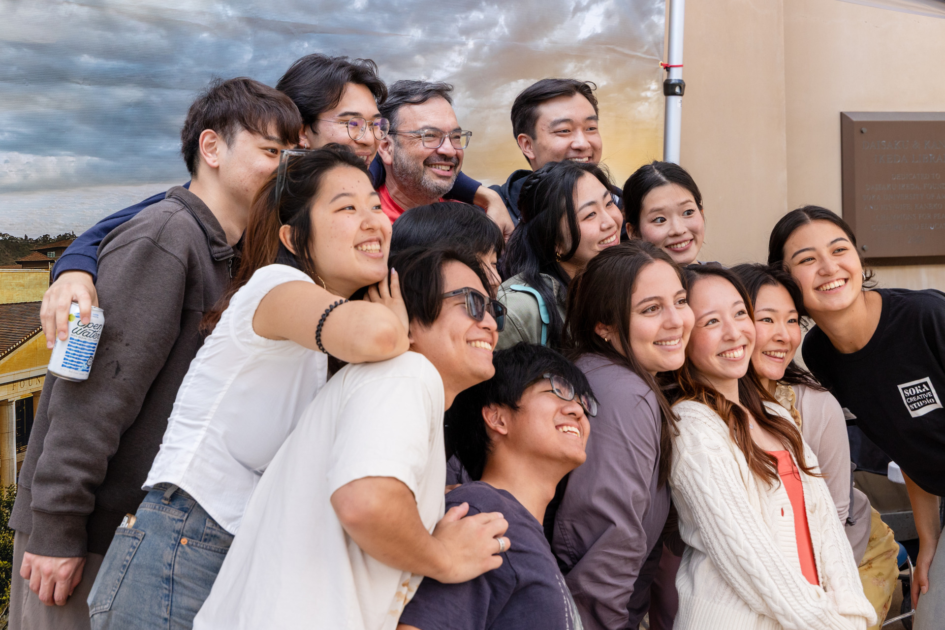 A large group of students and staff pose for a group photo in front of a backdrop during SUA's Homecoming celebration.