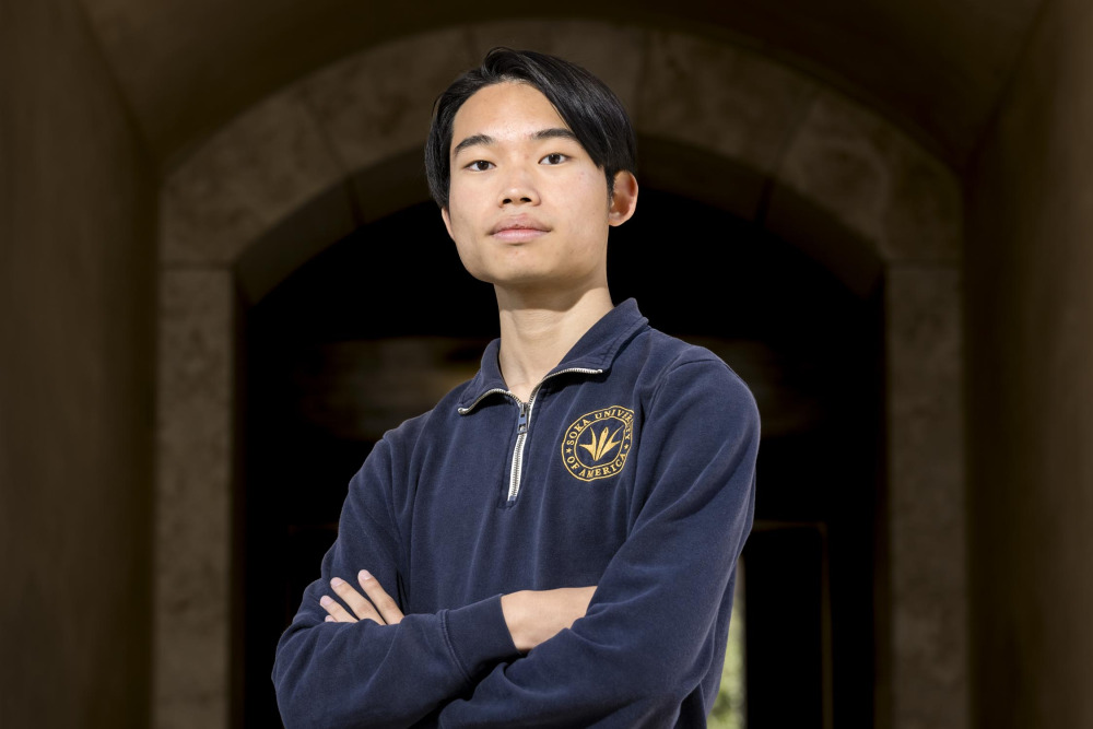 Shota Maeda ’27 wears a navy blue quarter zip with a gold Soka crest on the left chest. He stands with his arms crossed and looks at the camera.