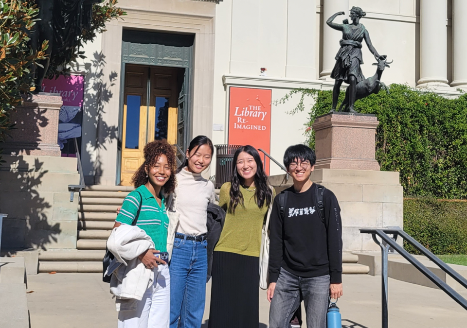 Four students stand in front a statue and steps.