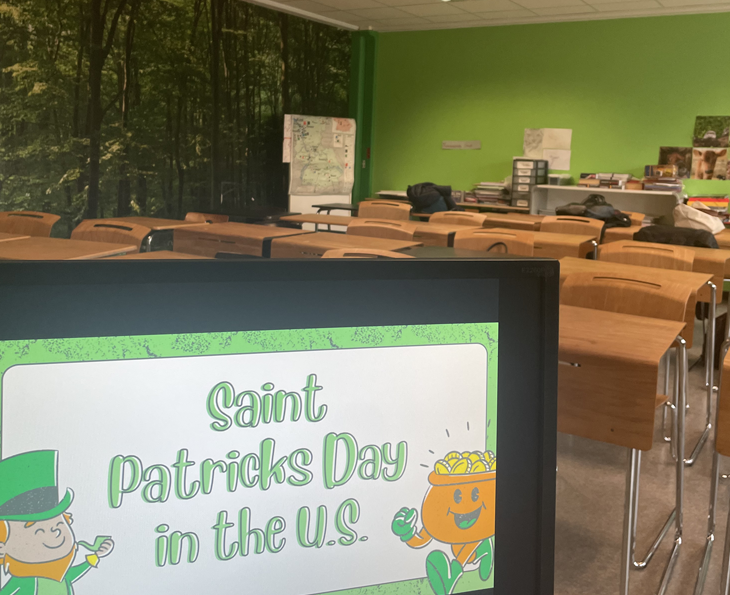 A sign reading "Saint Patricks Day in the US" is displayed at the entrance of a classroom with desks