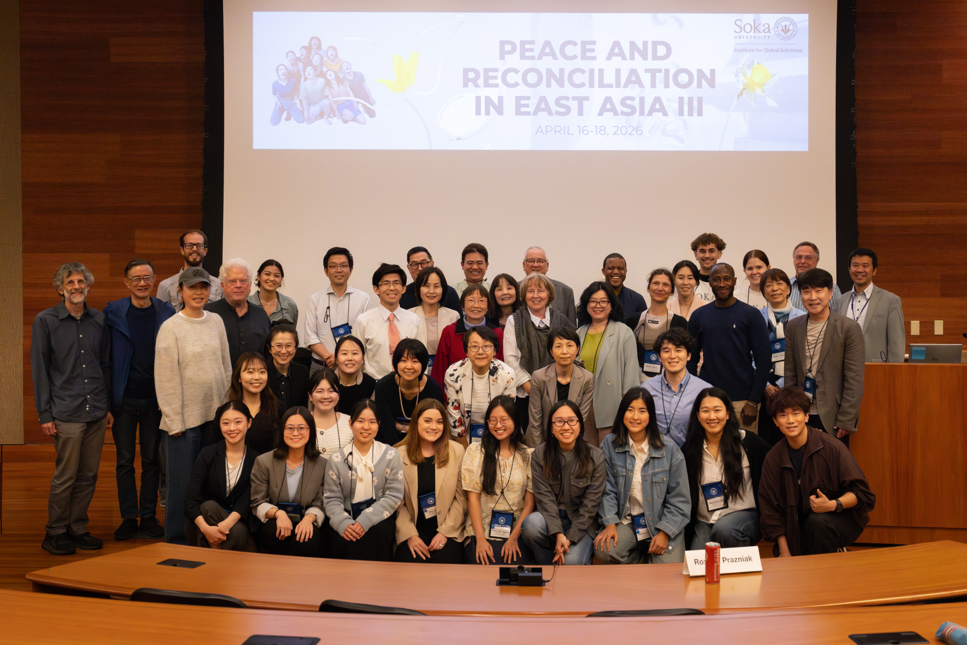 A large group photo of students, faculty, staff, and visiting scholars and student researchers in front of the white projector screen in the auditorium.