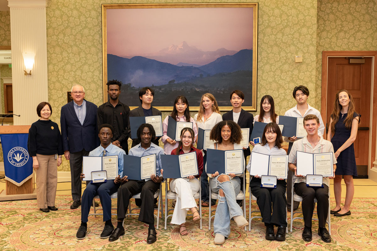 A large group of students hold up their academic awards and pose alongside university faculty and leadership.