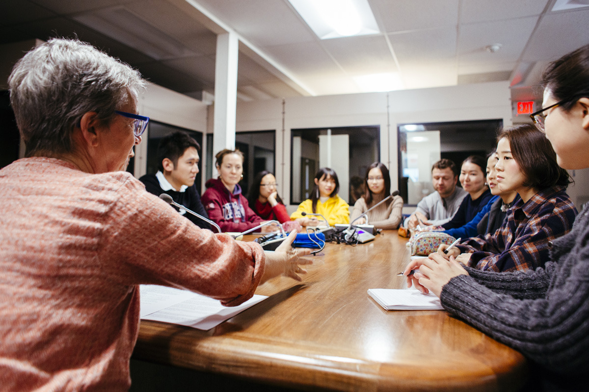 A group of 11 people sit around an oval wooden table and take part in a discussion.