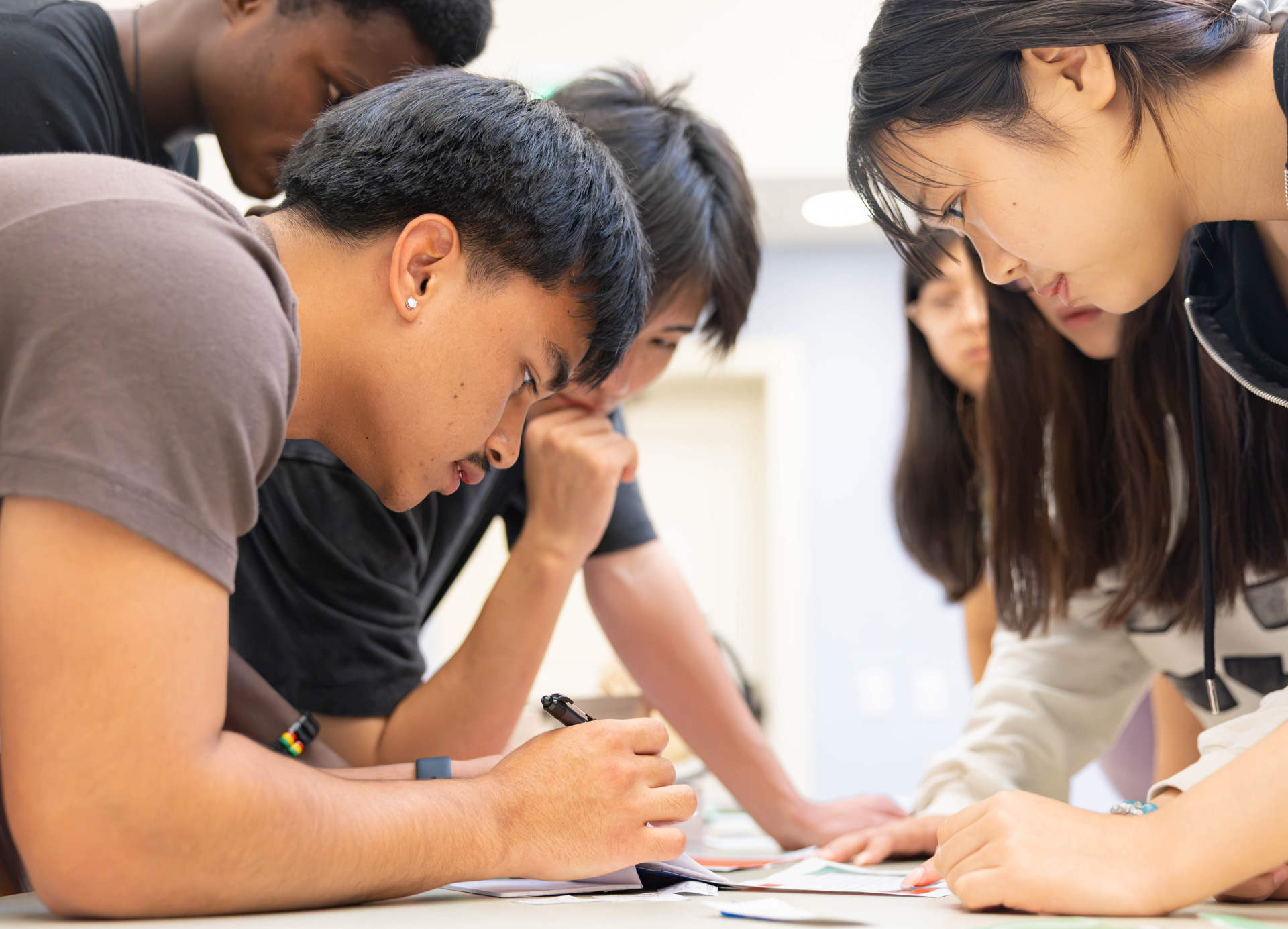 Male and female students lean in and look at items on a table during an escape room activity.