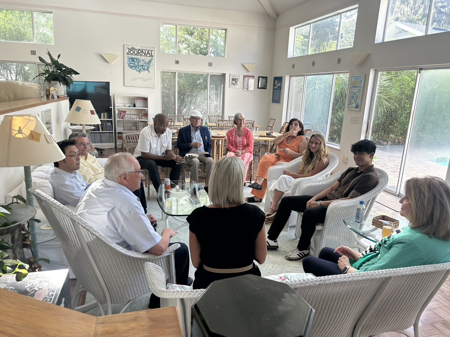 A group of people including college students and university leadership sit in a circle in a living room and engage in a discussion.