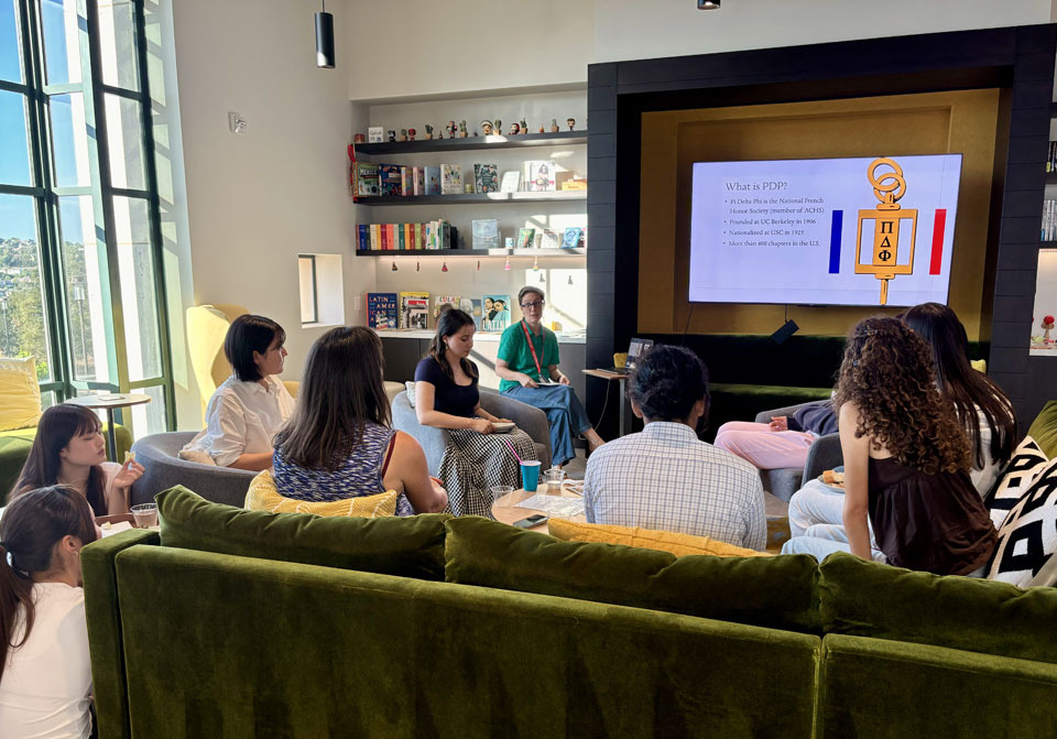 Students sit on a green couch and listen to a presentation about Pi Delta Phi.