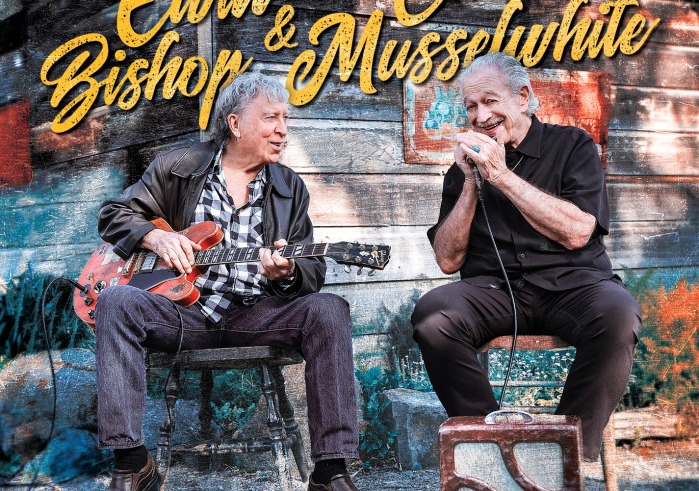 Two men sitting in chairs playing guitar and harmonica
