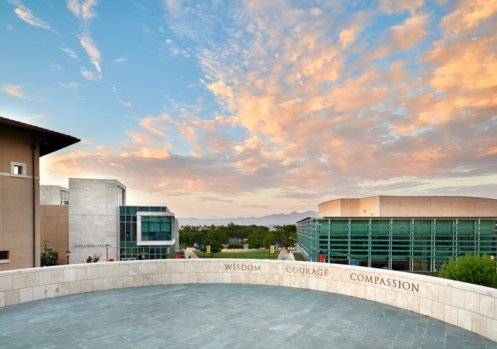 Central values of Soka University, Wisdom, Courage, and Compassion displayed on a wall in front of clouds and silhouetted mountains in the background