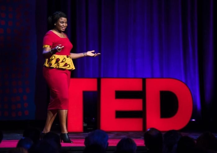 Professor Chika Esiobu stands in front of big red letters spelling out TED as she speaks on stage during her TED Talk