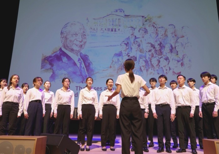 SUA student chorus signs the Light of Hope in front of drawing of Daisaku Ikeda 