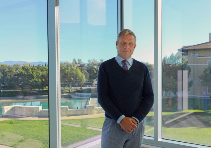 Dean Hamersley poses in front of glass windows on Soka University of America's campus
