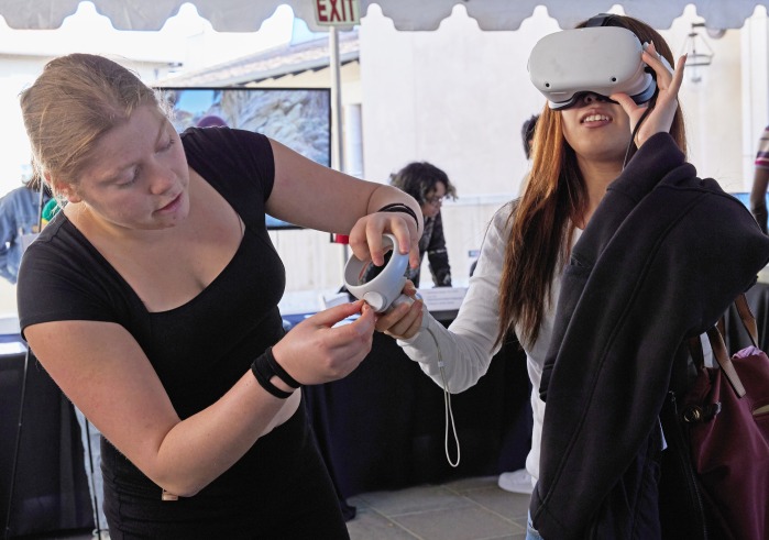 A woman wearing a VR headset is assisted by another woman.