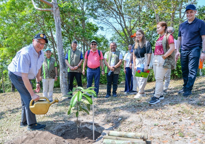 SUA President Ed Feasel waters a plant at the Soka Amazon Institute while a group of people look on