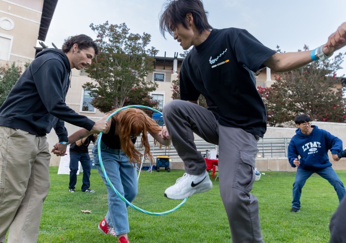 Students hold hands and try to move a hula hoop through a line of people as part of SUA's annual Welcome Back Community Event