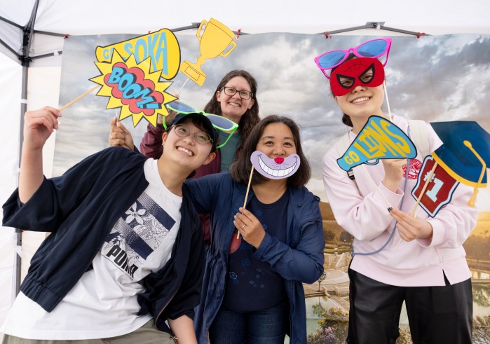Four people pose with props in front of an SUA campus backdrop during the 2025 Soka Homecoming event.