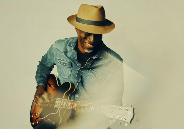 Man with hat in a blue shirt playing a guitar