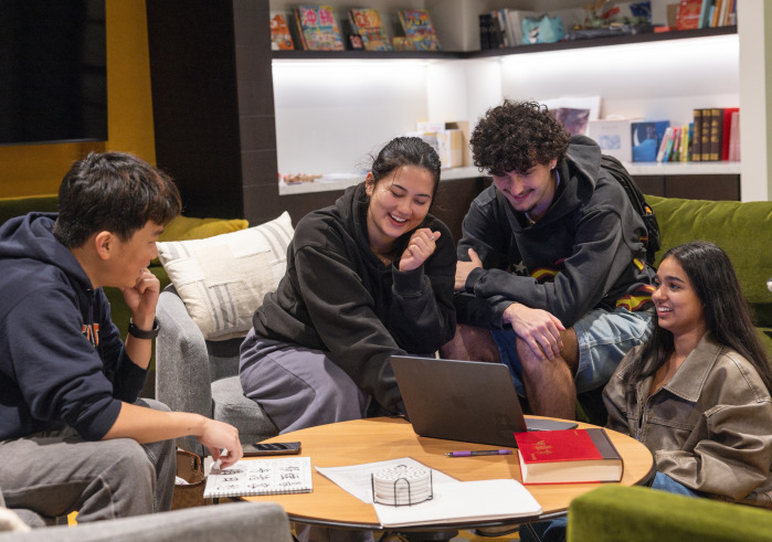 A group of students looking at a laptop, smiling and chatting in the language center