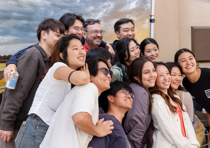 A large group of students and staff pose for a group photo in front of a backdrop during SUA's Homecoming celebration.