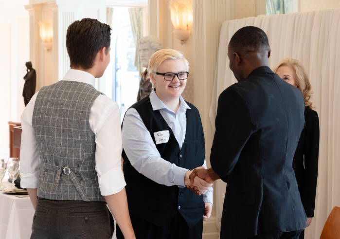 People dressed in business attire shake hands at an etiquette training event.