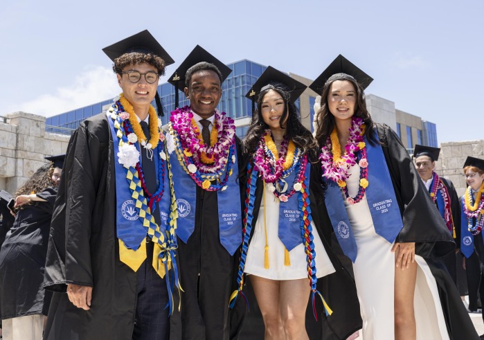 Four members of SUA's Class of 2025 smile in their cap and gown during commencement day.