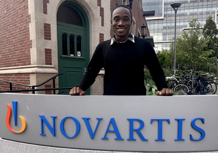 Edem Wordi ’27 poses behind a Novartis sign outside a brick building.