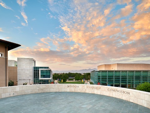 Central values of Soka University, Wisdom, Courage, and Compassion displayed on a wall in front of clouds and silhouetted mountains in the background