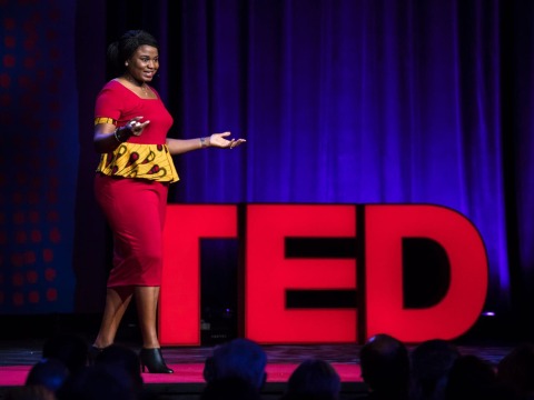 Professor Chika Esiobu stands in front of big red letters spelling out TED as she speaks on stage during her TED Talk