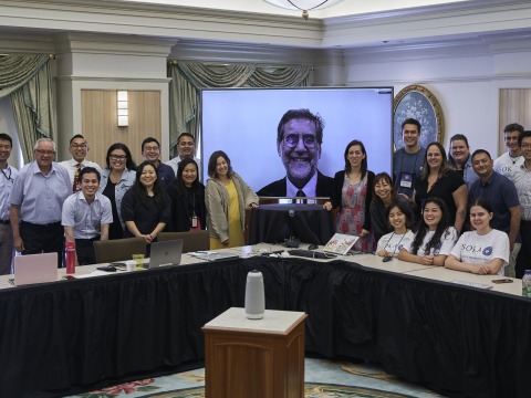 Members of SIGS pose for a photo in front of a tv screen featuring Andrea Bartoli, Executive Adviser of SIGS
