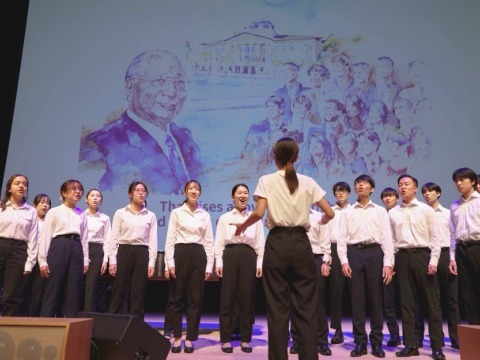 SUA student chorus signs the Light of Hope in front of drawing of Daisaku Ikeda 