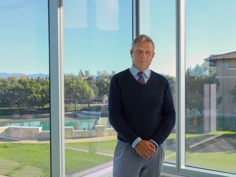 Dean Hamersley poses in front of glass windows on Soka University of America's campus