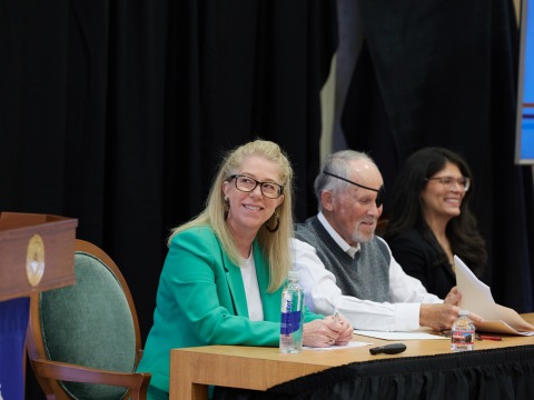 Three panelists sit at a desk together during the SBS Symposium
