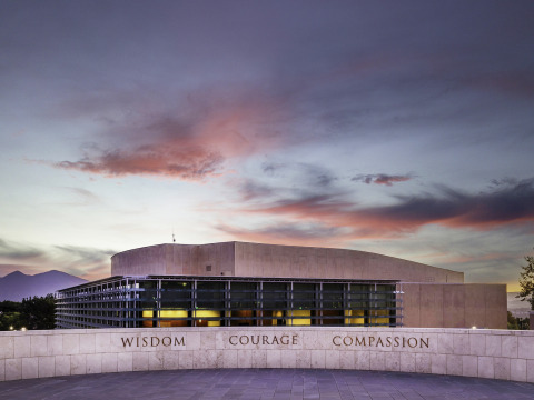 An overlook on SUA's campus displays the words "Wisdom, Courage, Compassion" in front of the Performing Arts Center which is lit up during dusk.