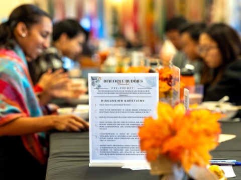 A "Dialogue Buddies" event features reflective questions on wellness and self-care, with participants gathered around a table decorated with orange flowers.