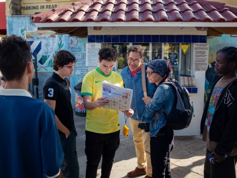 Six people stand together and look intently at a newspaper during a photo walk in Little Havana, Miami.