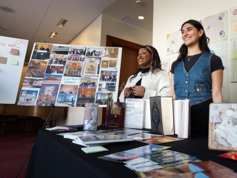 Two students smile as they stand with their research project during the winter block Learning Cluster Fair.