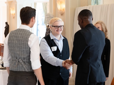 People dressed in business attire shake hands at an etiquette training event.