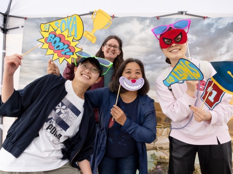 Four people pose with props in front of an SUA campus backdrop during the 2025 Soka Homecoming event.