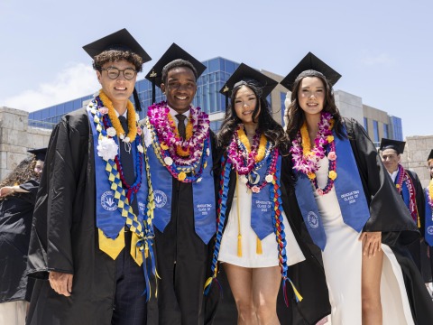 Four members of SUA's Class of 2025 smile in their cap and gown during commencement day.