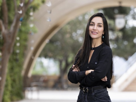 Foroogh Farhang crosses her arms and smiles at the camera outside on SUA's campus.