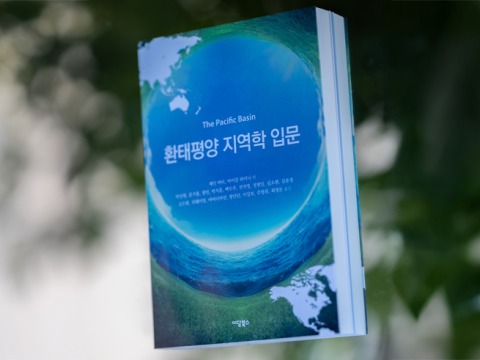 The textbook, “The Pacific Basin: An Introduction" is photographed in front of a white and green bokeh background.