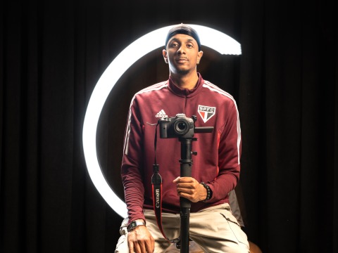 Lucas Colombo '27 holds a camera on a tripod and sits in front of a black backdrop.