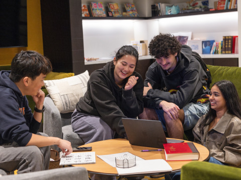 A group of students looking at a laptop, smiling and chatting in the language center
