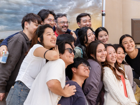 A large group of students and staff pose for a group photo in front of a backdrop during SUA's Homecoming celebration.