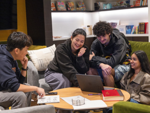 A group of students looking at a laptop, smiling and chatting in the language center