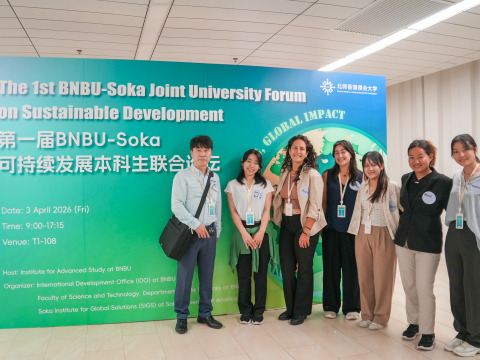 A man stands next to six women, all wearing nametags, as they pose in front of a large green and blue sign reading "The 1st BNBU-Soka Joint University Forum on Sustainable Development"